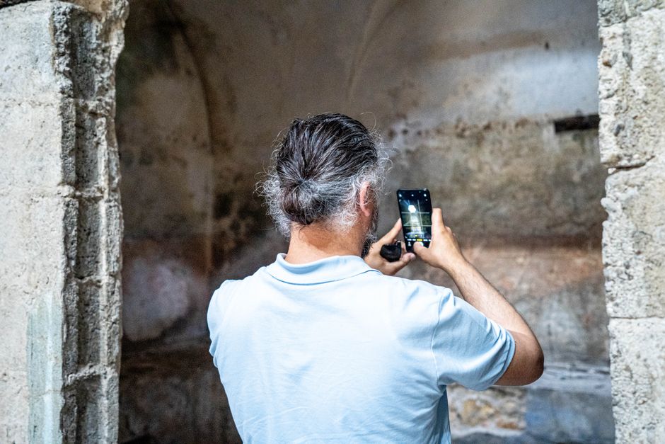 A man uses a smartphone to photograph ancient ruins indoors, capturing history through technology.